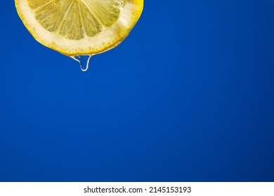 Fresh Slice Of Lemon Juice Drip On Blue Background, Citrus Dripping Isolated, Copy Space.