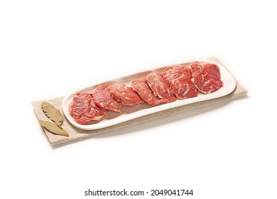 fresh sliced pork jowl in a white dish with some decorative spices and herbs close-up. isolated white background