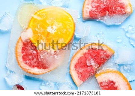 Fresh slices of citrus fruits frozen in ice on blue background