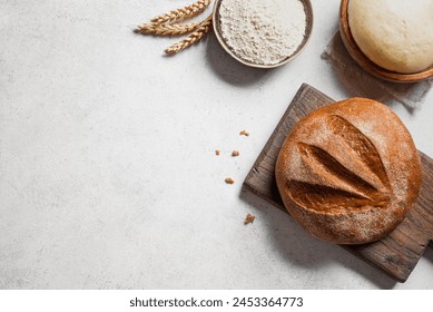 Fresh sourdough bread and ingredients. Loaf of bread on cutting board, ball of dough and flour on white table, baking background, copy space, banner. - Powered by Shutterstock