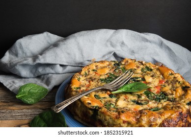 Fresh spinach with a homemade quiche on a rustic wooden table with dark background.  