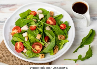 Fresh spinach salad with tomato, small pieces of herb roasted chicken in white ceramic dish on brown sackcloth, together with balsamic vinegar on white wooded table. Concept for healthy.