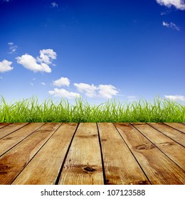 Fresh Spring Green Grass With Blue Sky And Wood Floor Background