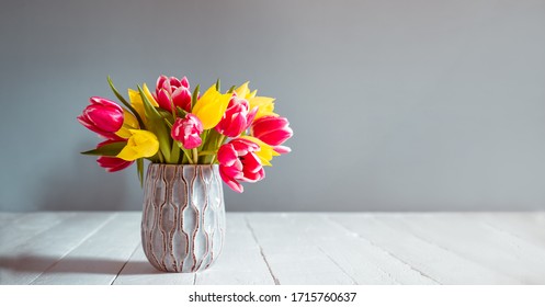 Fresh spring yellow and pink tulips bouquet in blue vase standing on black wooden table with gray background. Festive flowers for mother's or women's day. Mockup for greeting wide banner. Copy space - Powered by Shutterstock