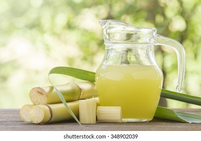 Fresh squeezed sugar cane juice in pitcher with cut pieces cane on nature background