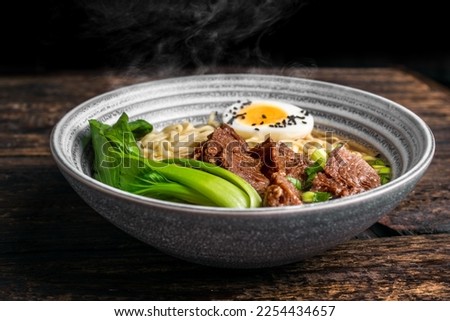 Fresh steaming beef ramen noodle soup serving with egg and pak choi, close up.