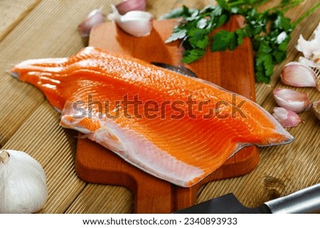 Fresh steelhead trout fillet on wooden surface with seasonings ready for cooking
