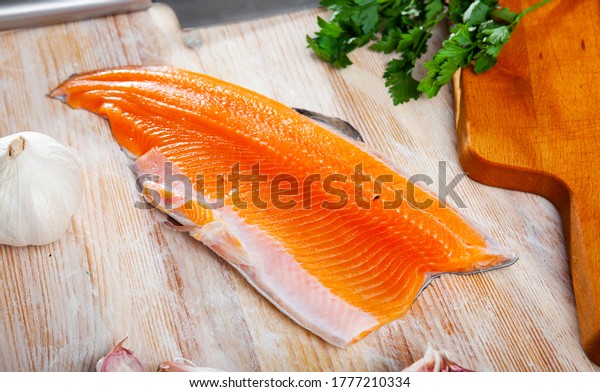 Fresh steelhead trout fillet on wooden surface\
with seasonings ready for\
cooking