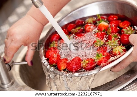 Fresh strawberries being washed in a sink under the tap of the water splashing around with shiny air bubbles and looking very fresh and clean.