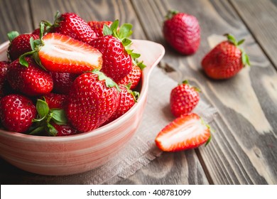 Fresh strawberries in a bowl on wooden table with low key scene.