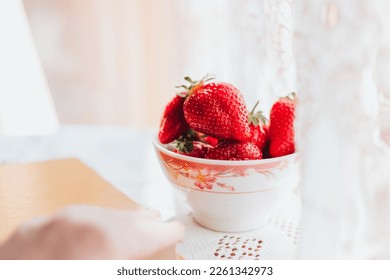 Fresh strawberries in the ceramic bawl on the table and a book. Morning leisure time