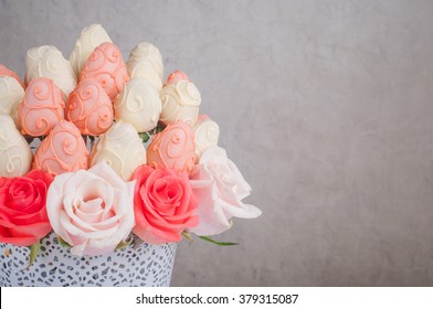 Fresh strawberry covered by pink and white chocolate with rose flowers designed as a fruit bouquet, grey wall as a background