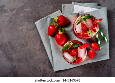 Fresh Strawberry Lemonade With Ice, Mint And Paper Straw In Sparkling Glasses On Gray Table Background, Copy Space. Cold Summer Drink. Berry Cocktail. Top View, Flat Lay, Overhead Shot