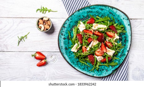 Fresh strawberry salad with arugula, strawberries and cheese brie, camembert. Plate with a keto diet food. Delicious breakfast or snack on a light background, top view. - Powered by Shutterstock