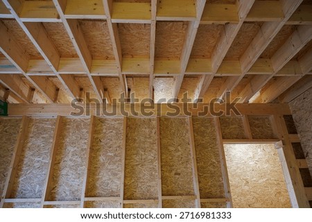 Fresh stud walls and ceiling joists of dimensional lumber with OSB sheathing are lit by construction lights, with an open doorway right and blocking showing load care.