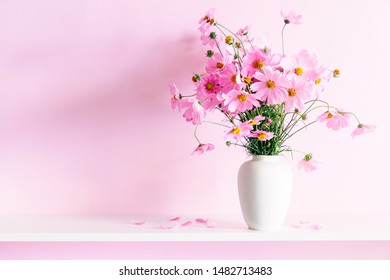 Fresh summer bouquet of pink cosmos flowers in white vase on white wood shelf on pink wall background. Floral home decor. - Powered by Shutterstock