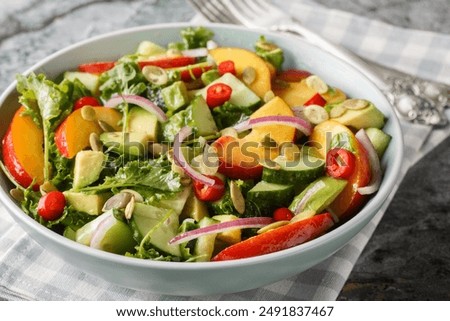Fresh summer salad with peach, avocado, cucumber, red onion, chili, arugula, spinach and pumpkin seeds close-up in a bowl on the table. Horizontal
