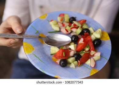 fresh summer vegetable salad with cucumbers tomatoes oleves garlic green on plate with hands and spoon close up photo