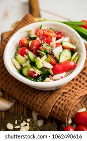 Fresh summer vegetables salad with tomatoes, cucumbers, onion, garlic, nuts in bowl. On wooden board. Organic farm products. White background. Raw, vegan, vegetarian healthy food