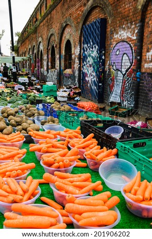 Fresh sweet carrots, potatoes, broccoli at Brick Lane market. Old building with graffities at backgrounds. London, UK.