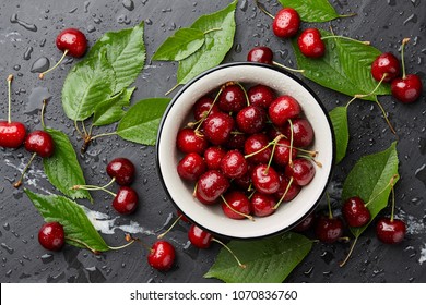 Fresh sweet cherries bowl with leaves in water drops on stone background, top view