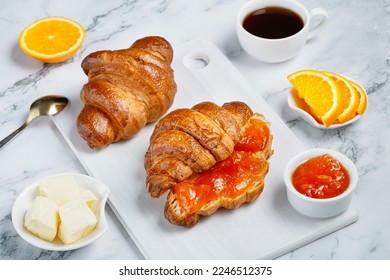 Fresh sweet croissants with butter and apricot jam for breakfast. Continental breakfast on a white concrete table