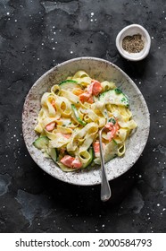 Fresh tagliatelle pasta with salmon and zucchini in cream sauce on a dark background, top view