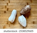 Fresh taro roots on a rustic wooden cutting board. Two roots are peeled, showcasing their creamy interior, perfect for culinary creations.