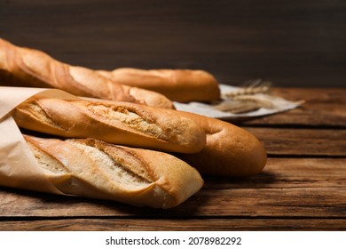 Fresh tasty baguettes and spikelets on wooden table, closeup