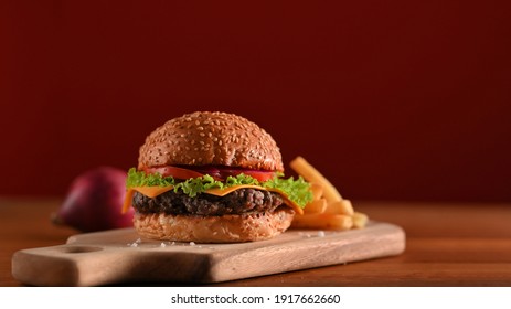 Fresh tasty beef burger and french fries served on wooden tray on the table in fast food shop with red wall background