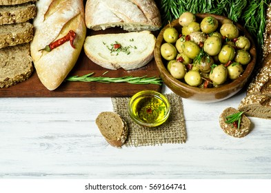 Fresh tasty olives placed with variety of baked bread,rosemary and organic olive oil for delicious snack on white wooden background.Top view,Copy space..