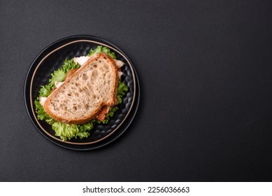 Fresh tasty sandwich with chicken, tomatoes and lettuce on a black plate on a dark concrete background - Shutterstock ID 2256036663