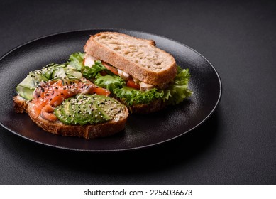 Fresh tasty sandwich with salmon, avocado and sesame and flax seeds on a dark concrete background - Shutterstock ID 2256036673