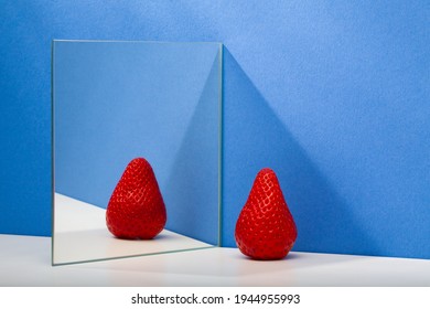 A fresh and tasty strawberry reflected in the mirror on the blue background. Fresh strawberry in the mirror reflection. Juicy strawberry.