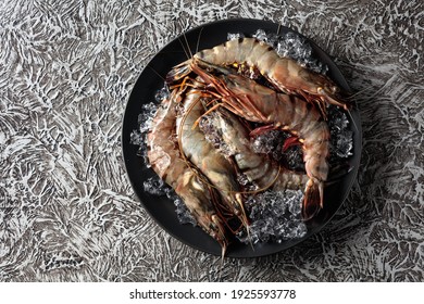  Fresh tiger prawns in a black plate with crushed ice on rough rustic background, top view with copy space.