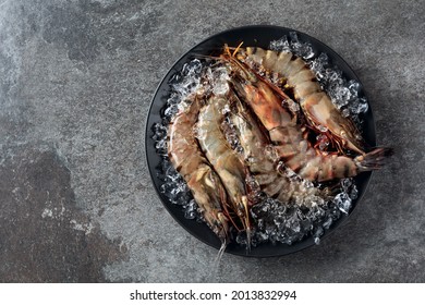  Fresh tiger prawns in a black plate with crushed ice on rough stone background, top view with copy space.