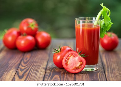 fresh tomato juice in glass with celery stick and heap of ripe vegetables on wooden table outdoors