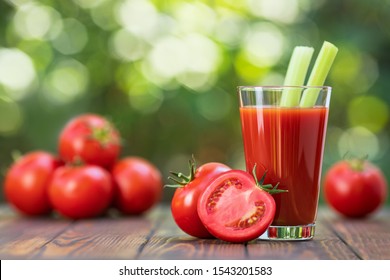 fresh tomato juice in glass with celery sticks and heap of ripe vegetables on wooden table outdoors
