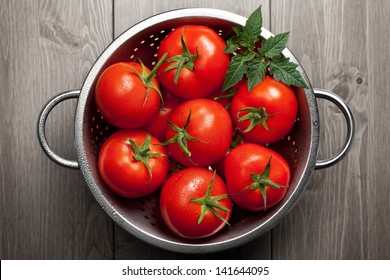 Fresh tomatoes with green leaf and waterdrops in colander on wooden background. Top view - Powered by Shutterstock