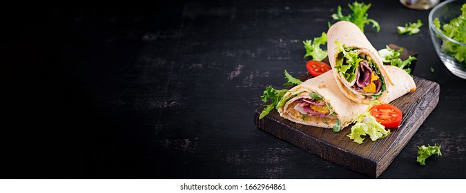 Fresh tortilla wraps with ham beef and fresh vegetables on wooden board. Beef burrito. Mexican cuisine. Banner