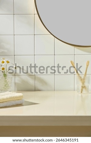 Fresh towel stack, toothbrushes, and small vase of daisies against white tiled wall. Bright daylight and clean counter emphasize simplicity and elegance in a serene bathroom setup.
