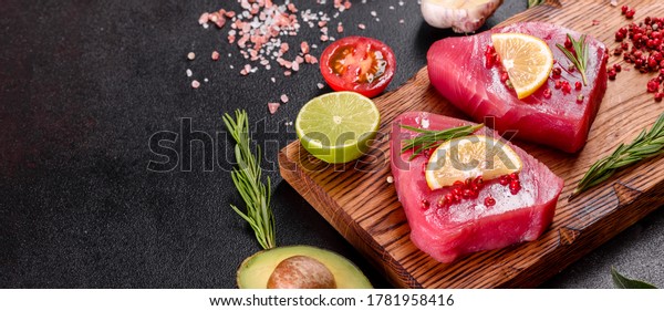 Fresh tuna fillet steaks with\
spices and herbs on a black background. Preparing tuna for\
baking