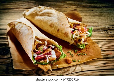 Fresh Turkish doner kebabs in toasted tortilla wraps served on brown paper on a rustic wooden table in a close up view