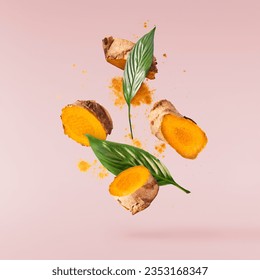 Fresh turmeric root with powder and green leaves falling in the air isolated on pink background. Food levitation conception. High resolution image.