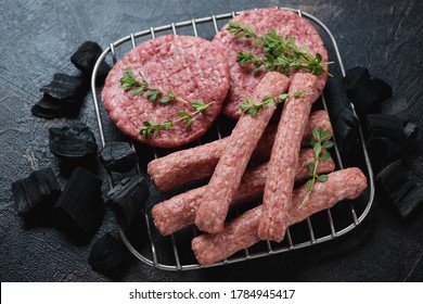 Fresh uncooked balkan cevapi or skinless beef sausages with pljeskavicas or meat patties on a metal rack with charcoals, studio shot