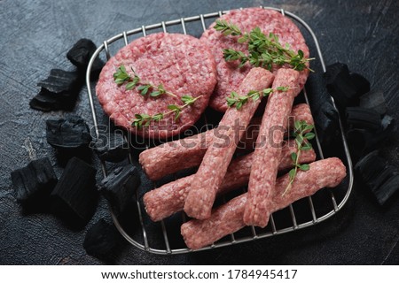 Fresh uncooked balkan cevapi or skinless beef sausages with pljeskavicas or meat patties on a metal rack with charcoals, studio shot