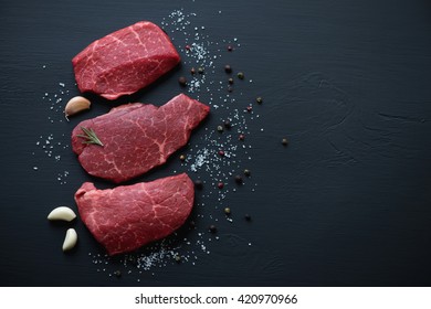 Fresh uncooked marbled beef schnitzels on a black wooden surface, above view