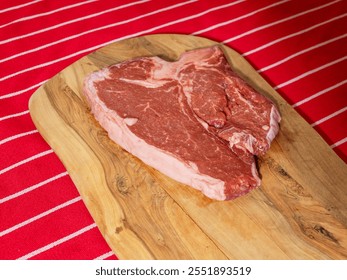 Fresh uncooked T bone steak on a wooden cutting board and on classic red and white stripe table cloth. High quality beef meat product. Butcher craft. - Powered by Shutterstock