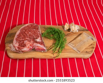 Fresh uncooked T bone steak with fresh dill and garlic clove and sauce in a plastic pouch on classic red and white stripe table cloth. High quality beef meat product. Butcher craft. - Powered by Shutterstock