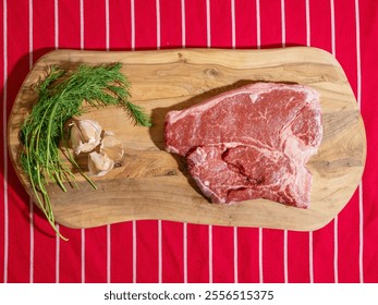 Fresh uncooked T bone steak with fresh dill and garlic cloves on wooden cutting board and on classic red and white stripe table cloth. High quality beef meat product. Butcher craft. - Powered by Shutterstock